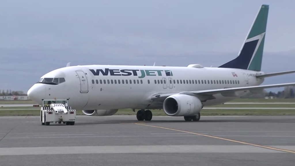 A WestJet plane sits on the tarmac at Vancouver International Airport with cloudy conditions in the background