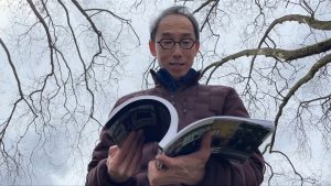 man wearing glasses and red puffer jacket holds book and flips through it Henry Tsang is an author and historian that focuses on the anti asain riots of 1907 in Vancouver.