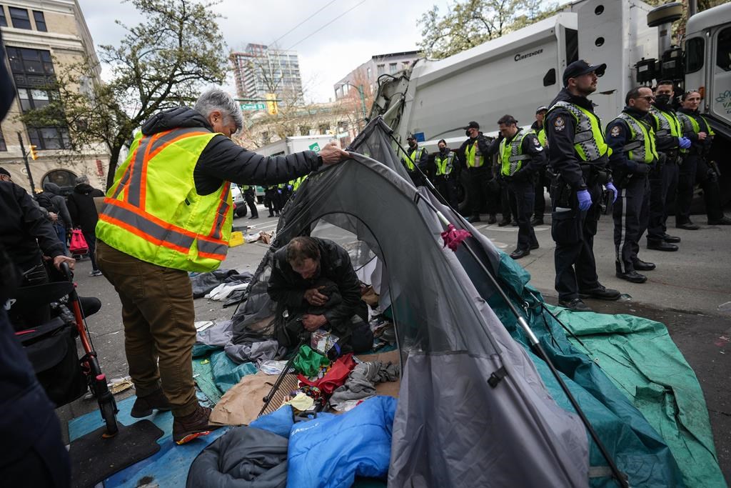 A man is seen inside his tent as police officers stand by while city workers clear an encampment on East Hastings Street in the Downtown Eastside of Vancouver, Wednesday, April 5, 2023