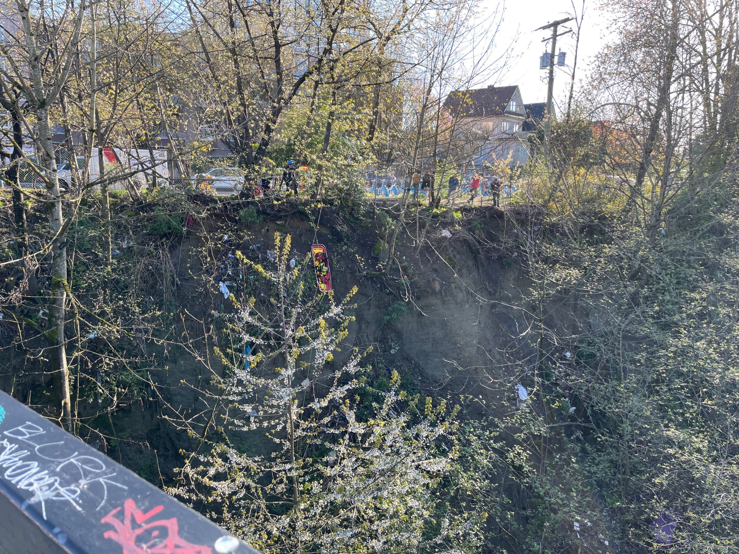 Fire crews send rescue gear down a forest bank next to a bridge.