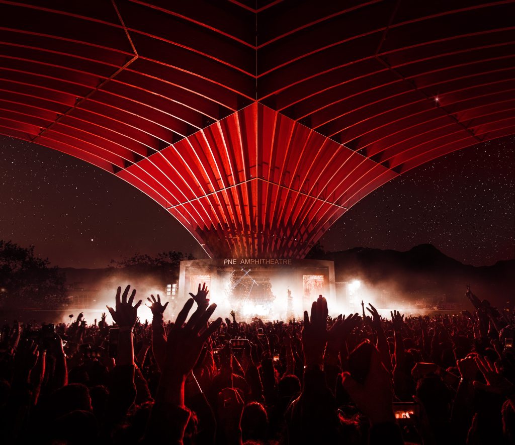 a concert concept for vancouvers pne amphitheatre. The theatre is lit up in red with smoke and hands raised in the air are seen as what a concert might look like.