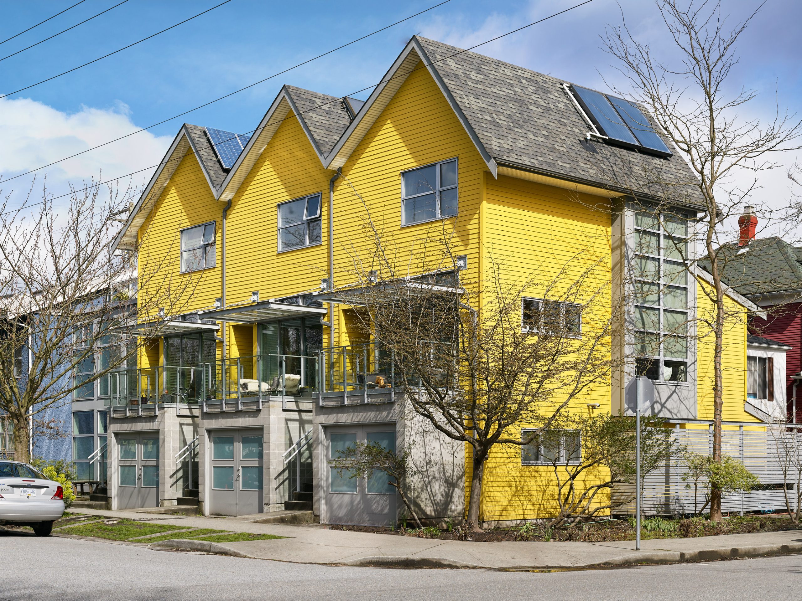 Three heritage houses are seen lining the corner of a block on a sunny day.