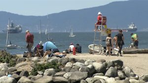 people on the beach, sitting on logs in vancouver. spending time in the sun during vancouvers heatwave