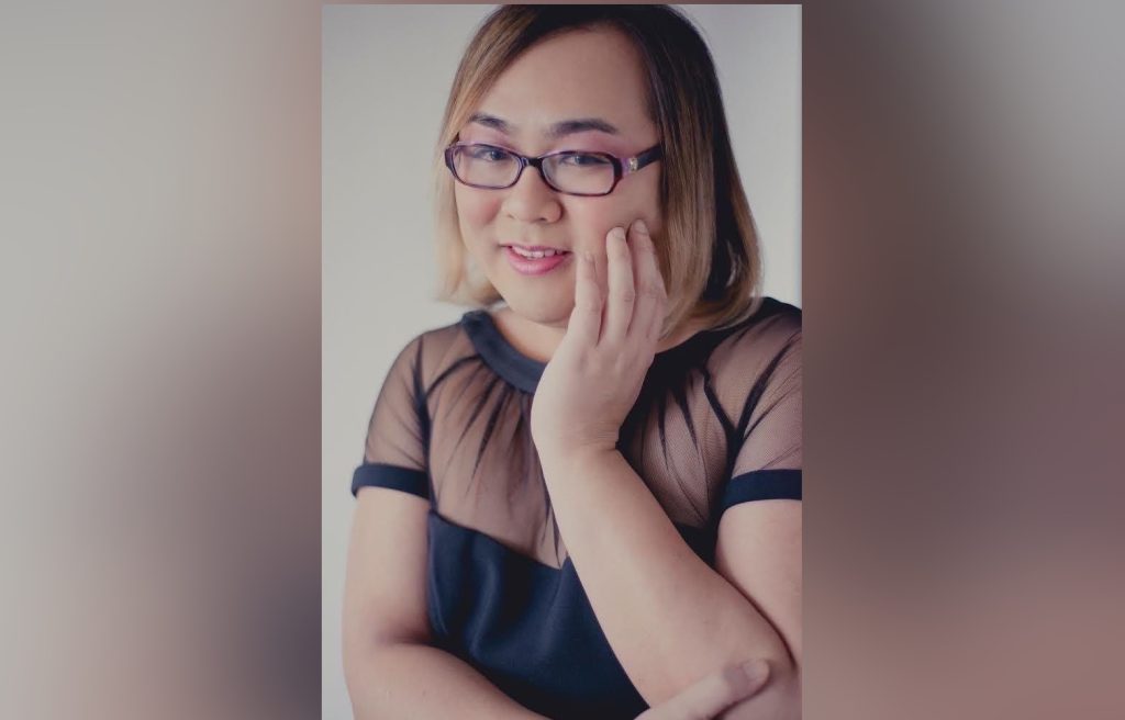 a woman stands with her hand touching her face and smiles. Transgender stand-up comedian Robin Tran is scheduled to headline the Asian Takeover Comedy Show at Vancouver's Vogue Theatre on Friday.