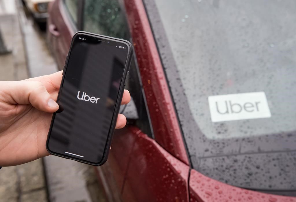 a black cell phone shows the uber logo in front of a red car with an uber sign in it.
