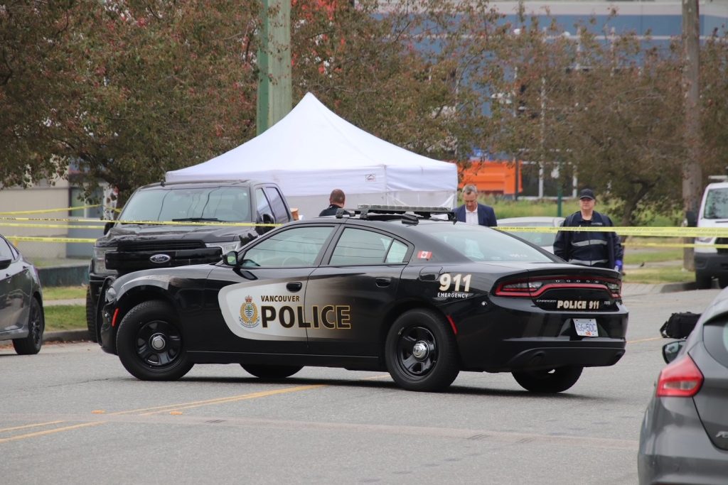 two police cruisers at a vancouver crime scene with a white tent seen in the distance