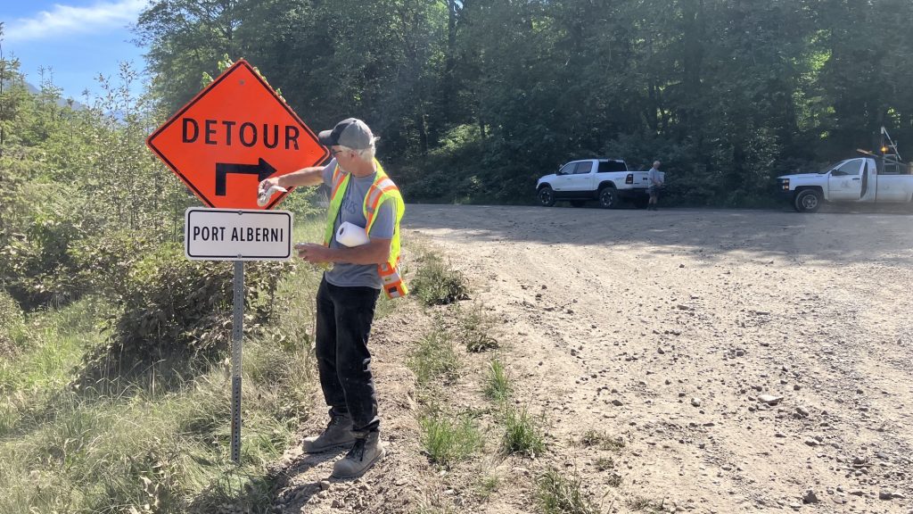 A man stands next to a detour sign near Port Alberni on a gravel road