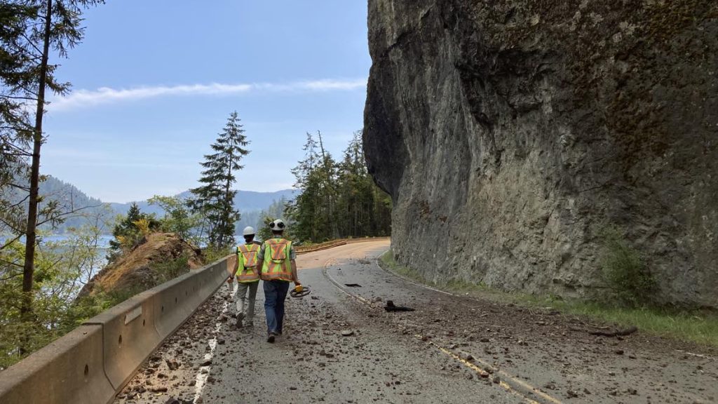 Highway workers walk along Highway 4 near Cameron Lake, the road is scattered with rocks and debris