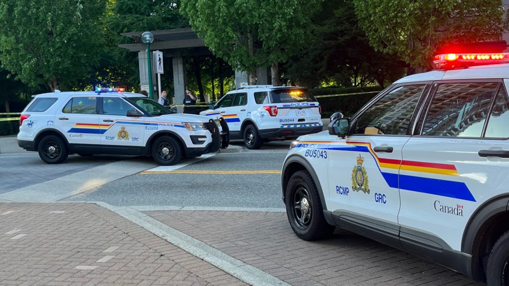 Police vehicles are seen on a road, with crime scene tape blocking an area