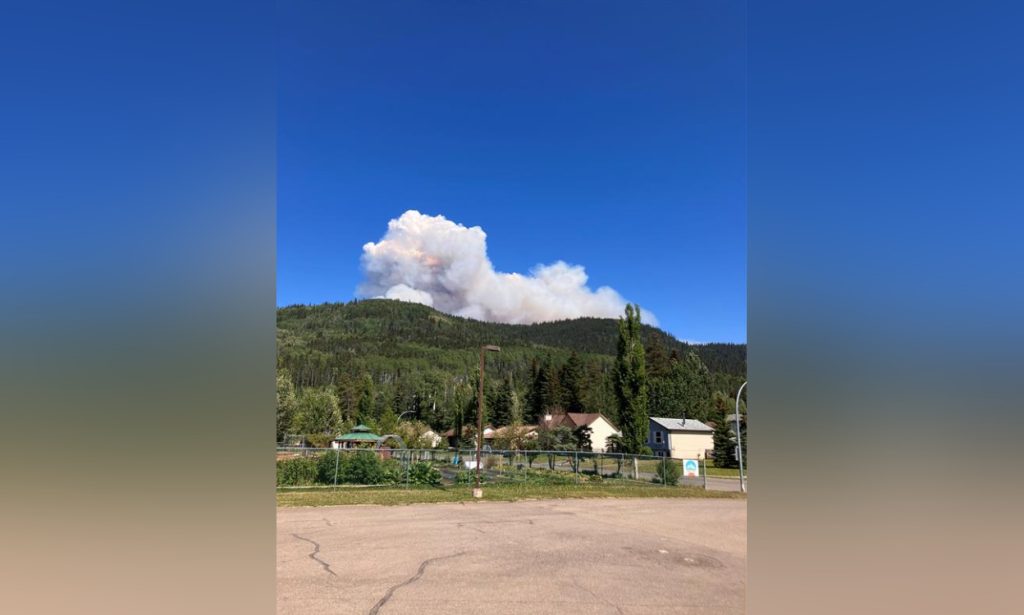 a plume of white smoke seen over a hill due to a large wildfire burning near tumbler ridge