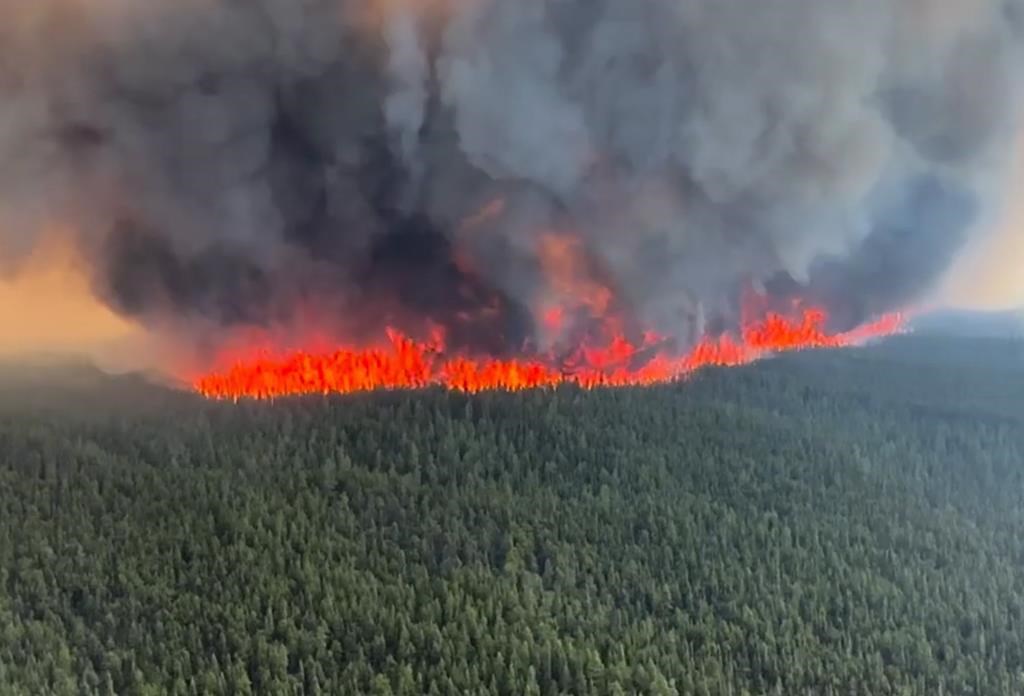 a large wildfire seen burning in northern bc red flames and black smoke plume from the blaze