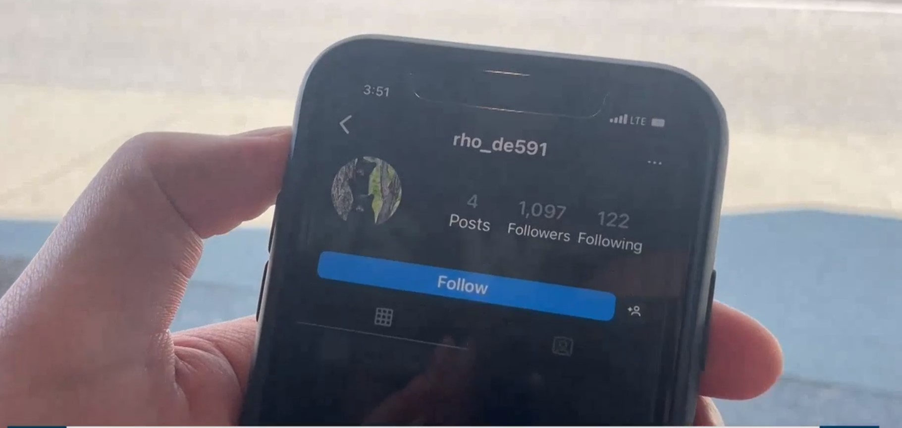 a person holds up a cell phone displaying an instagram profile 
