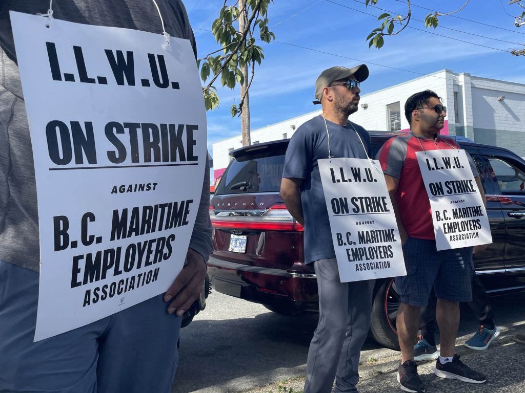 people hold up white signs on the picket line as port workers in bc resumed a strike after a tentative agreement deal was rejected