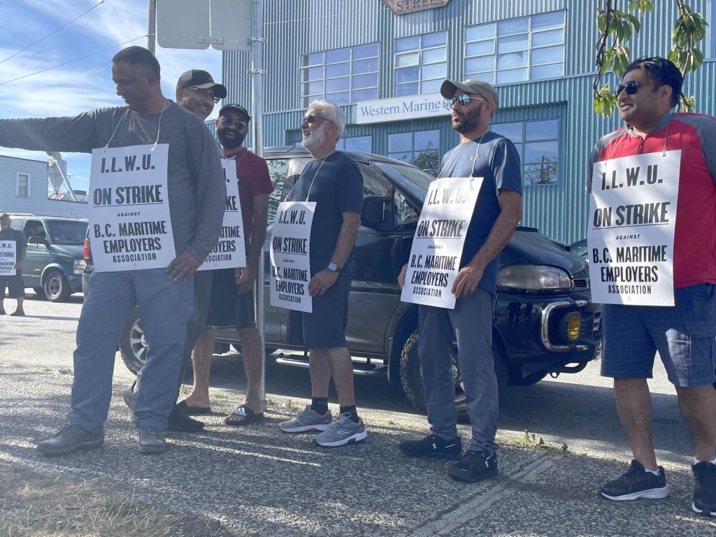 people hold up white signs on the picket line as port workers in bc resumed a strike after a tentative agreement deal was rejected