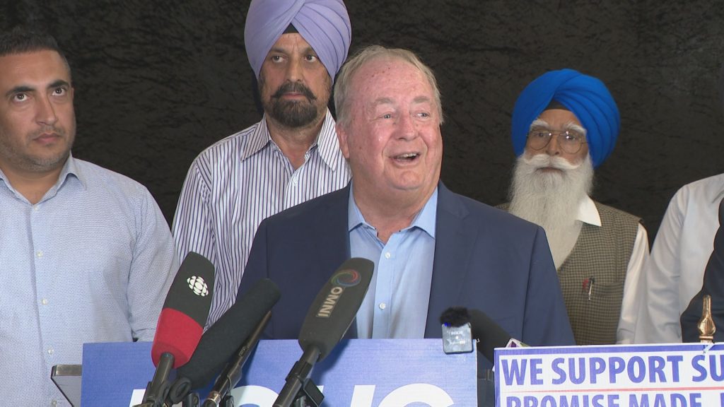 Doug McCallum stands at a podium during a press conference with a smile on his face