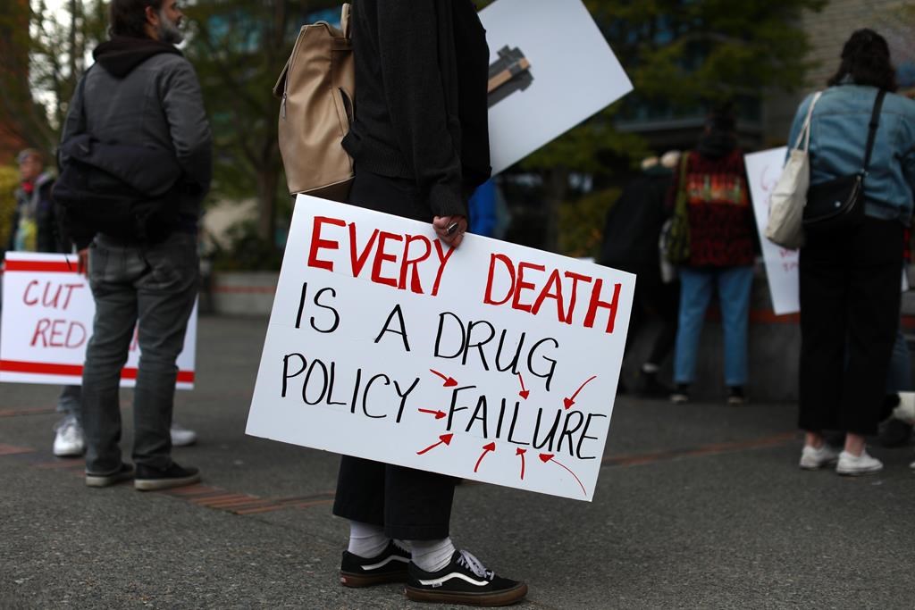 A protester holds a sign during a rally in Victoria, Thursday, April 14, 2022. The BC Coroners Service says 184 people died in B.C. in June due to the toxic, unregulated drug supply that has claimed more than 1,200 lives in the first six months of 2023. The coroners service says the numbers show just how risky it continues to be for users who access their drugs on the illicit market.