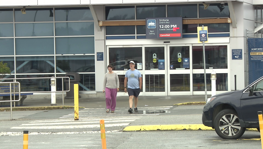 Passengers walk out of the Tsawwassen Ferry Terminal, where a sign shows a noon sailing is cancelled due to mechanical issues with the Coastal Celebration.