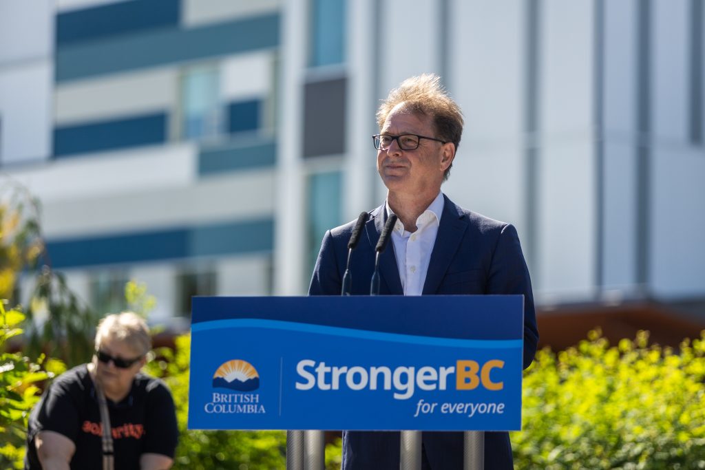 Health Minister Adrian Dix stands outside at a podium that reads "Stronger BC"