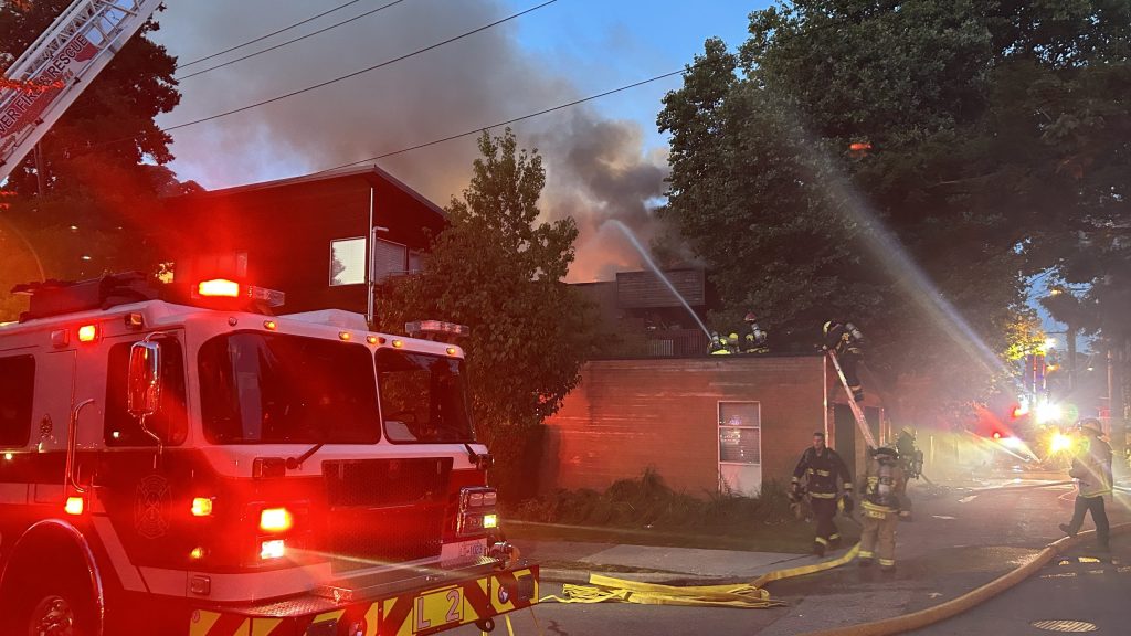 Fire engine on scene with crews on a roof putting out a fire