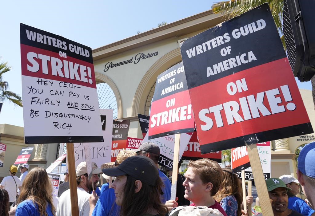 Striking Hollywood writers hold up signs while they picket outside a studio