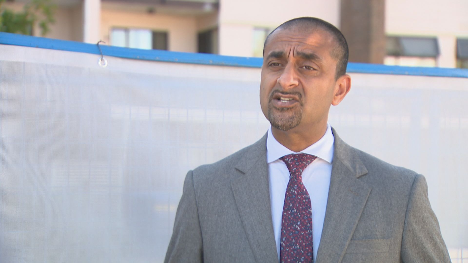 Ravi Kahlon speaks in front of a white fence