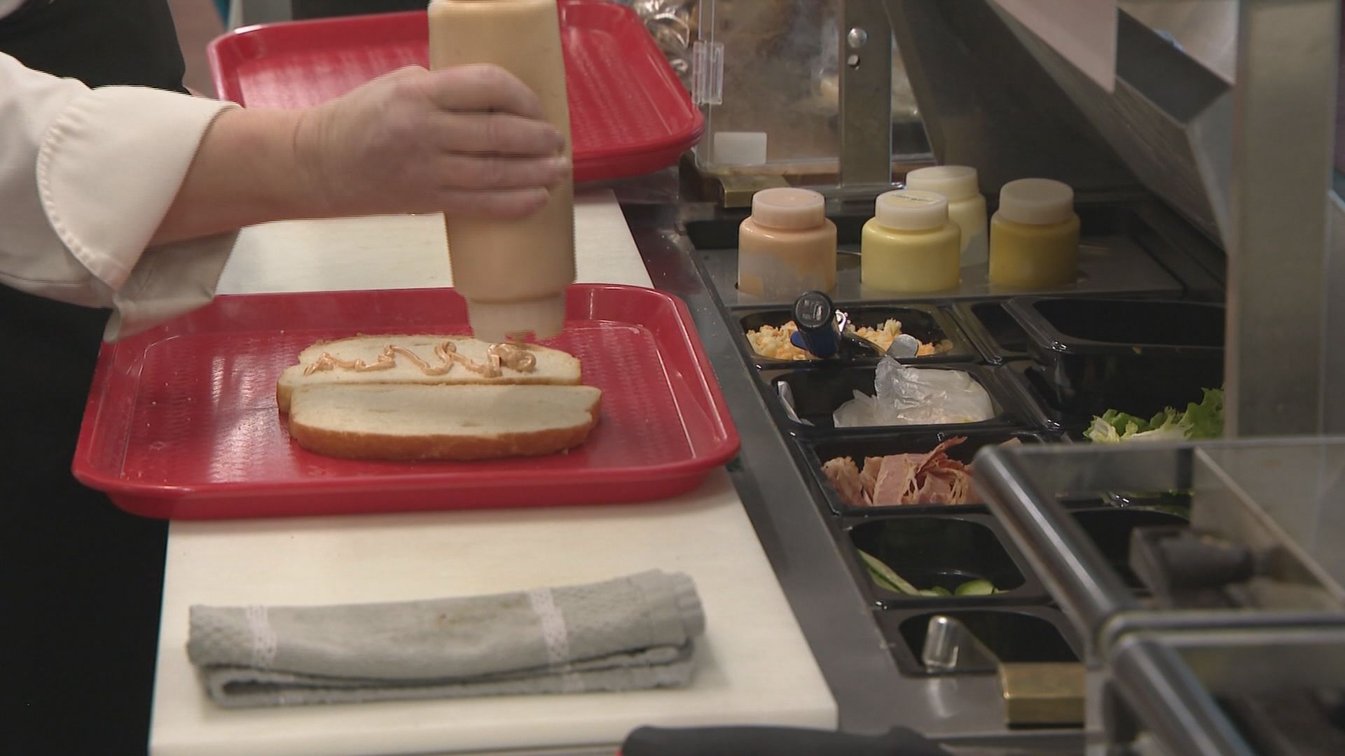A sandwich is being made on a bun on a tray. Other sauces and ingredients are laid out nearby.