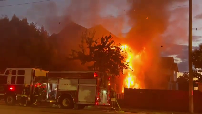 A fully-involved house fire is glowing orange with a fire truck responding in the foreground