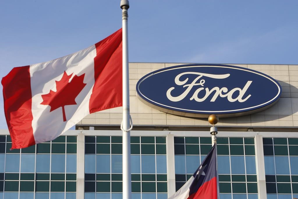 A Canadian flag flutters in the wind near a Ford logo