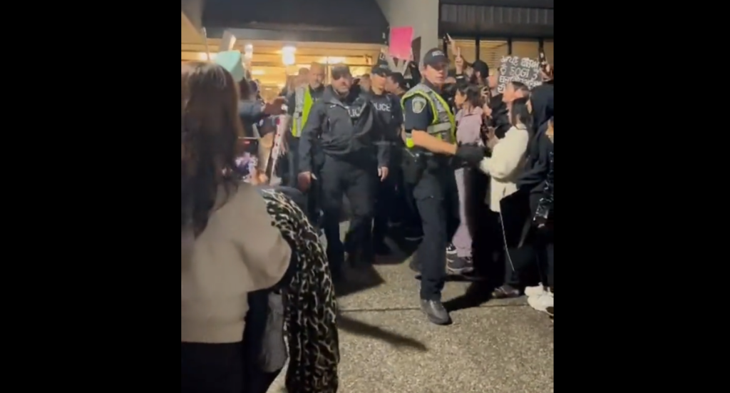 Abbotsford police officer escort school trustees out of a board meeting through a large crowd of anti-SOGI protesters