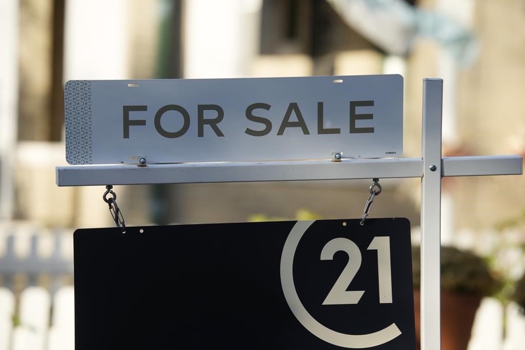 A for sale sign stands outside a single-family home