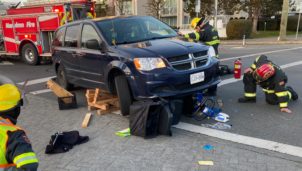Crews in Nanaimo work at removing a mobility scooter from under a minivan.
