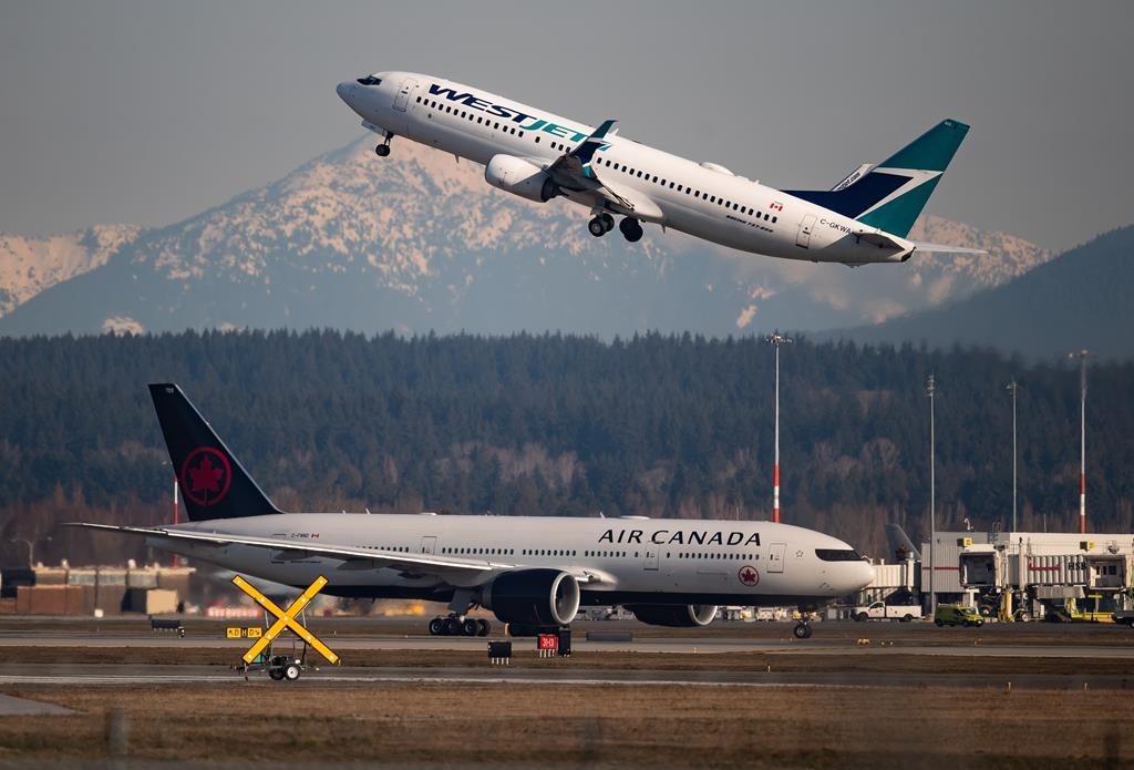 An Air Canada flight taxis to a runway as a WestJet flight takes off at Vancouver International Airport, in Richmond, B.C., on March 20, 2020.