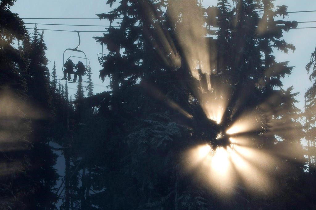 Skiers go up in a chairlift as the sun is framed through the trees on Blackcomb mountain in Whistler, B.C., Sunday, Dec, 11, 2011. British Columbia's abnormally warm winter has left local ski resorts grappling with the lack of snow during the crucial holiday tourism season, as resorts struggle to keep runs open.