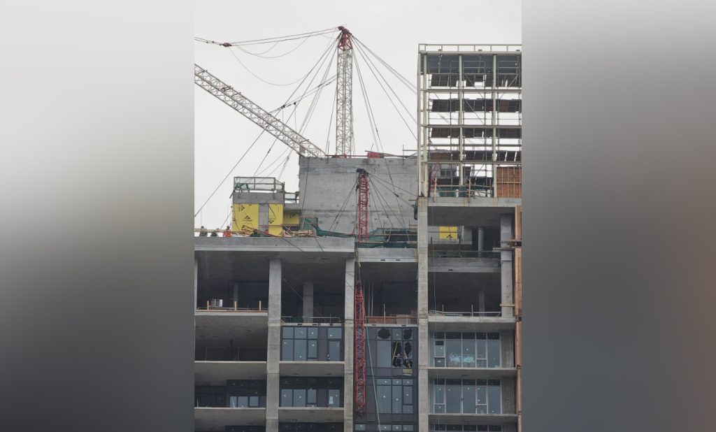 A piece of a crane is seen hanging off the side of a building under construction in Burnaby, along Lougheed Highway near Gilmore Street