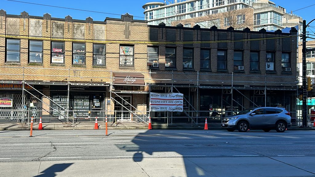 A banner outside a heritage building in the area of E Broadway and Kingsway says businesses are open on Feb. 12, 2024. The sign was still up despite the stores being forced to close days prior due to structural concerns with the building's façade. 