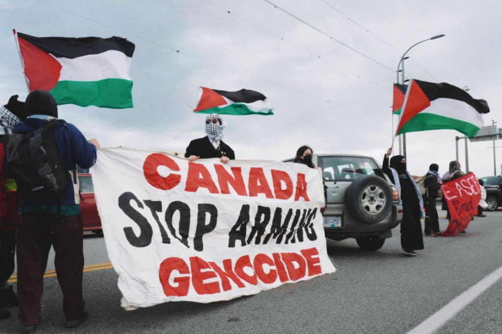 Protesters hold up a sign that reads "Canada stop arming genocide" as part of the "People's Picket for Palestine" protest at the Deltaport on April 15, 2024