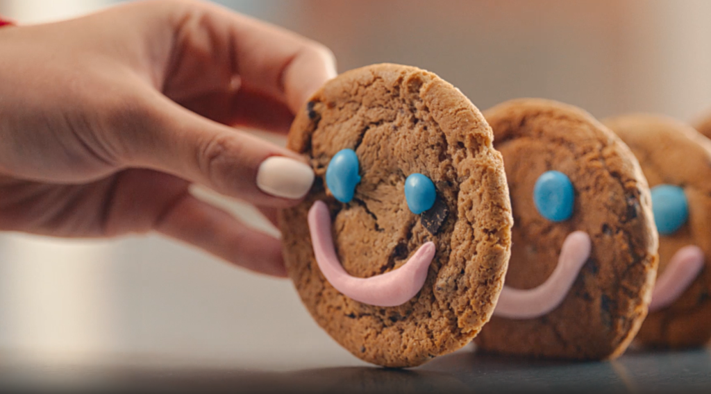 Close up of a hand holding a cookie decorated with a smiley face.