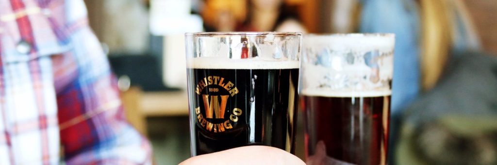 Close up of a glass of beer with the Whistler Brewing Co. logo printed on it.