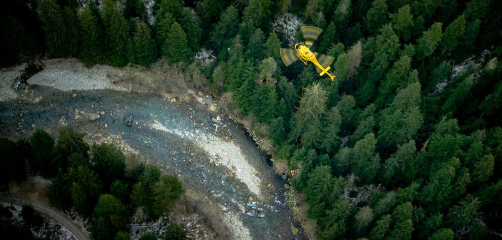 A helicopter flies over a river in a B.C. forest