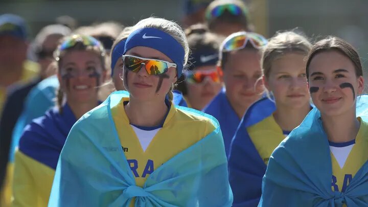 The Ukrainian Junior Women's Softball team stand together covered by flags