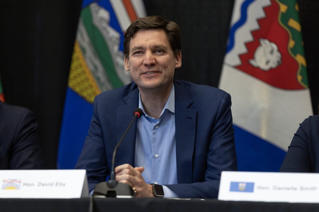 David Eby sits in front of provincial flags