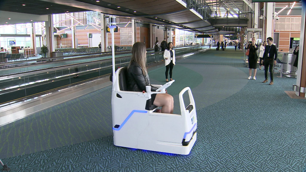 A woman sits in a white mobility scooter robot at the airport