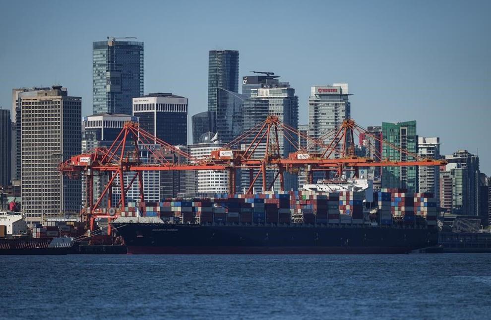 A container ship docked under gantry cranes at port and the downtown skyline are seen in Vancouver