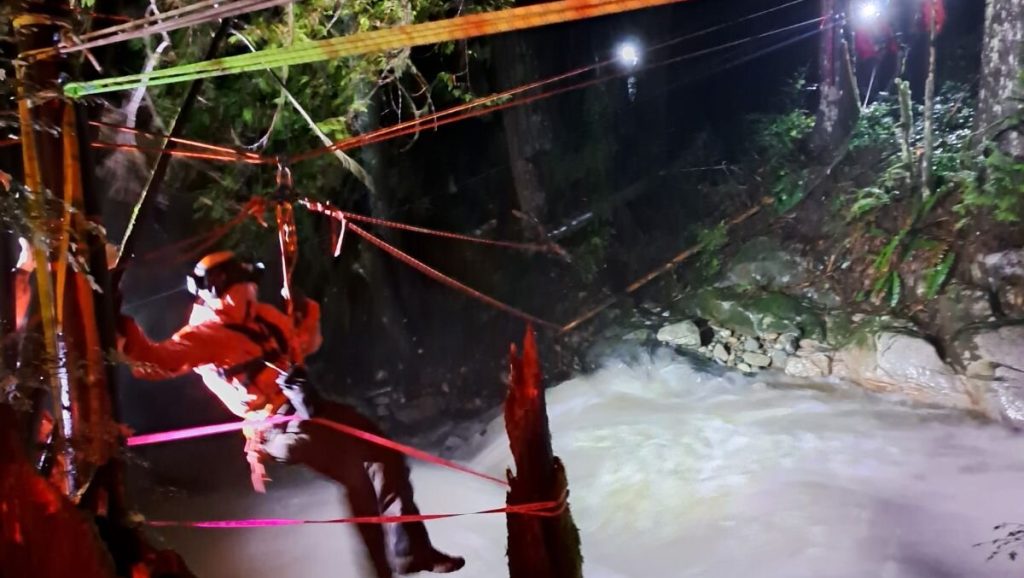 A CSR member nagivates highline tethers over rapid flowing water in the dark