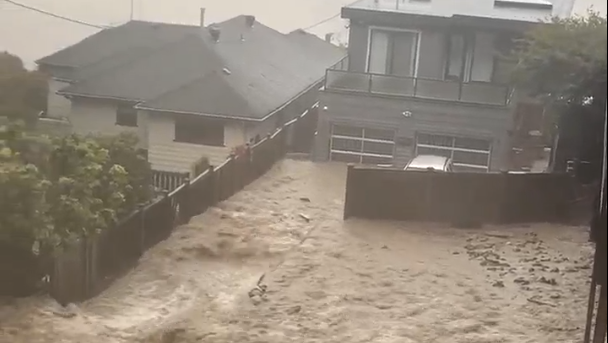 flood waters pour over a yard in Deep Cove