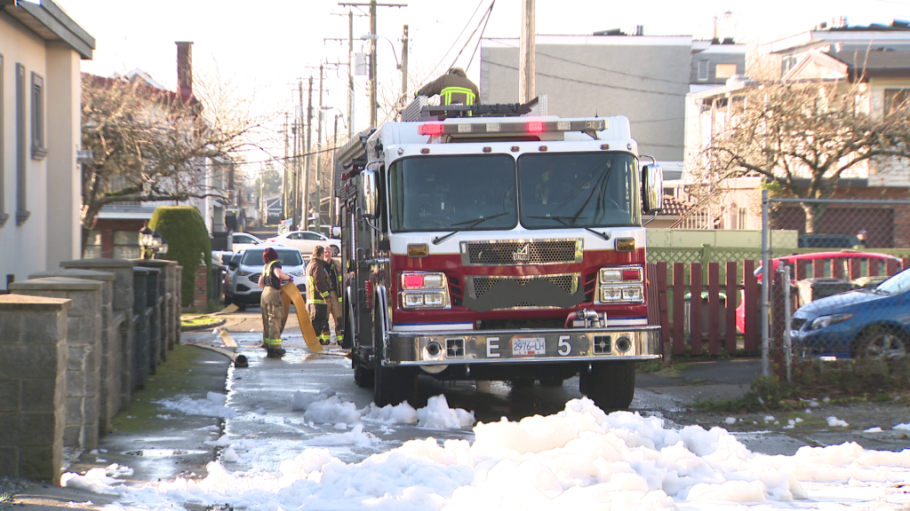 Fire crews stand outside an East Vancouver home partially destroyed by fire