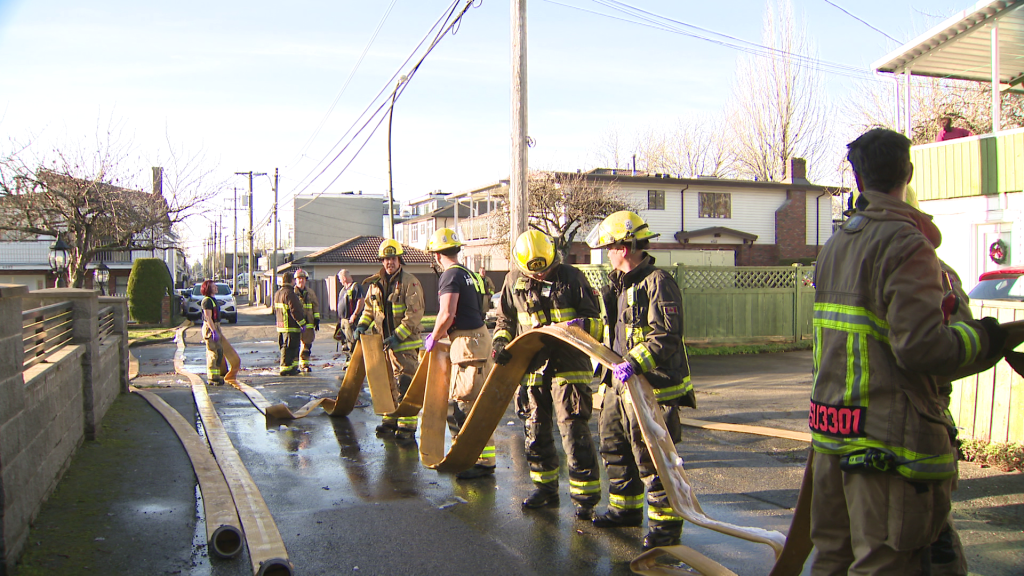 Firefighters stand outside an East Vancouver home partially destroyed by fire