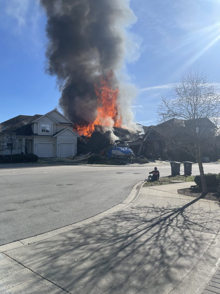 A man sits and watches a house fire