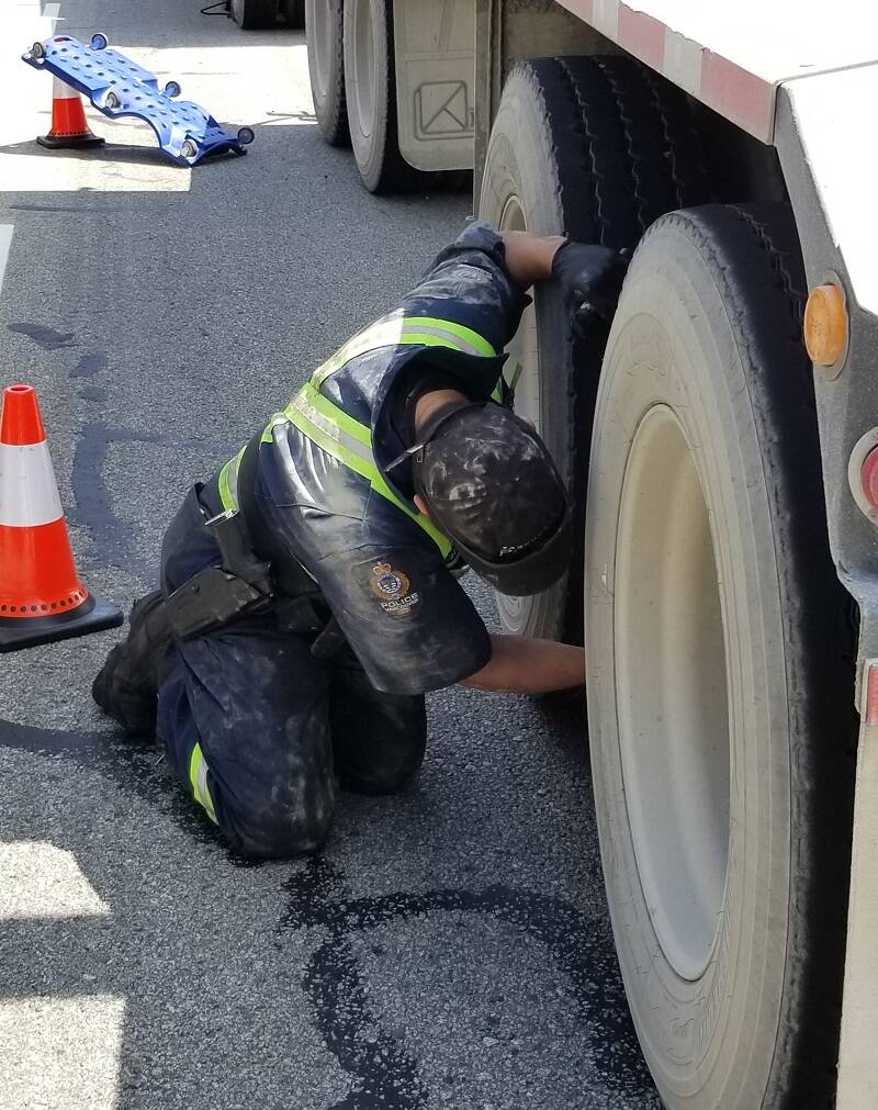 A commercial vehicle inspector inspects a tire on a truck.