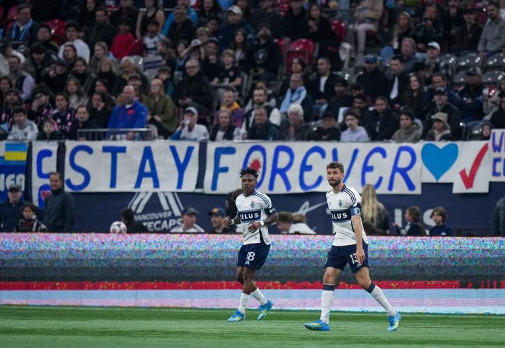 Vancouver Whitecaps' Thomas Muller and Edier Ocampo watch the play as a banner urging the team to stay in Vancouver is displayed behind them during the first half of an an MLS soccer match against Sporting Kansas City, in Vancouver